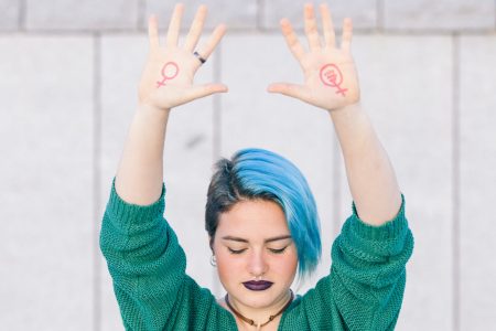 strong teen young woman fighting for gender equality with the feminist symbol on both hands isolated on the street