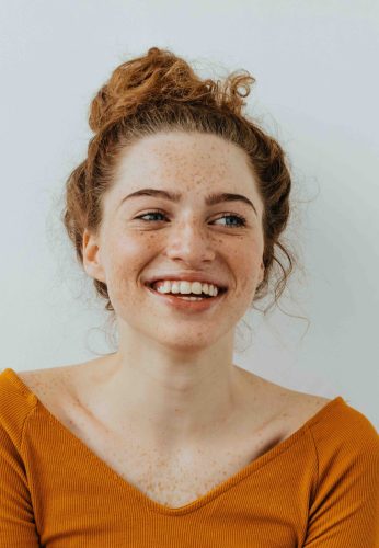 Happiness. Beautiful blue eyed girl with freckles is looking away and laughing, on a white background